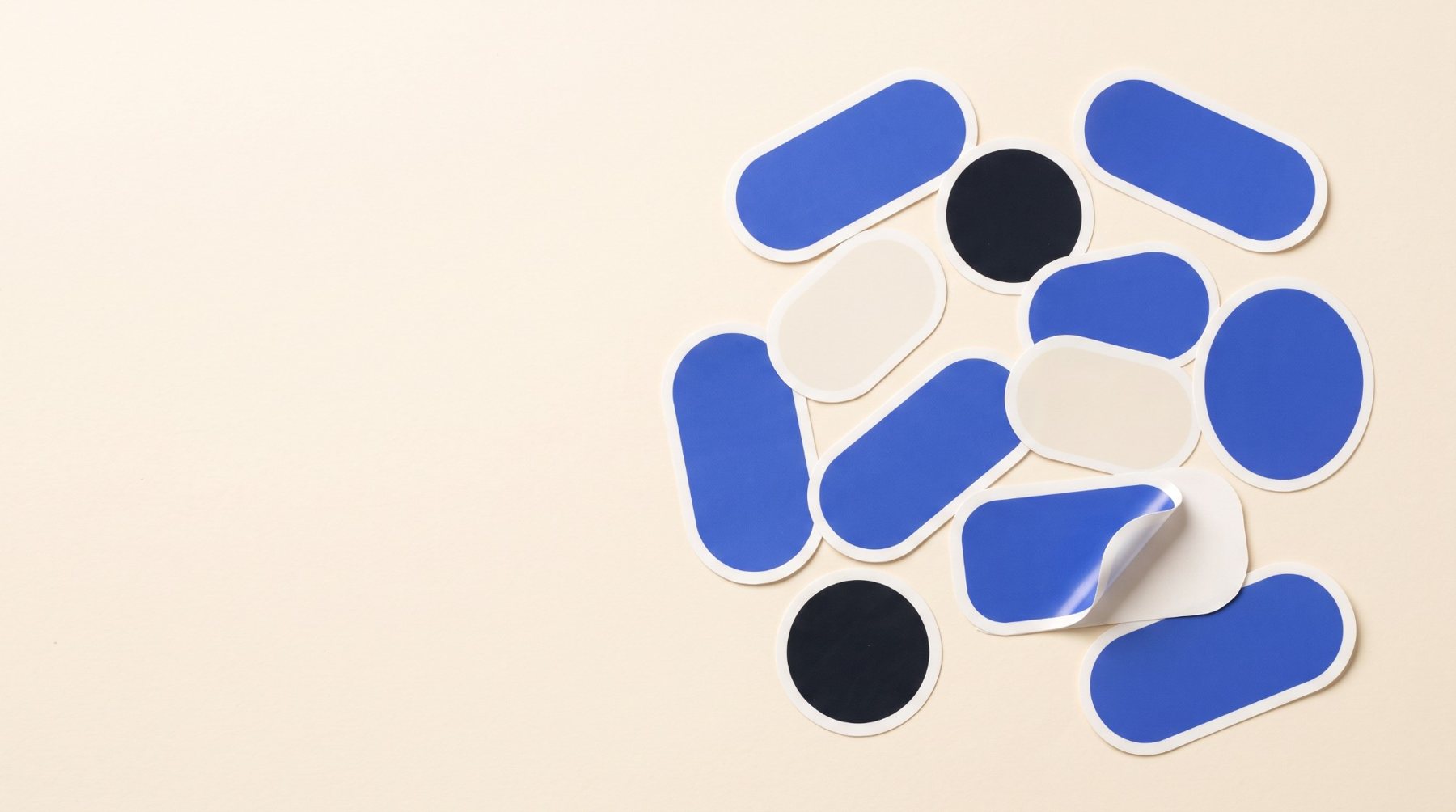 Blank die-cut vinyl stickers in blue, black and cream, one peeling from its backing