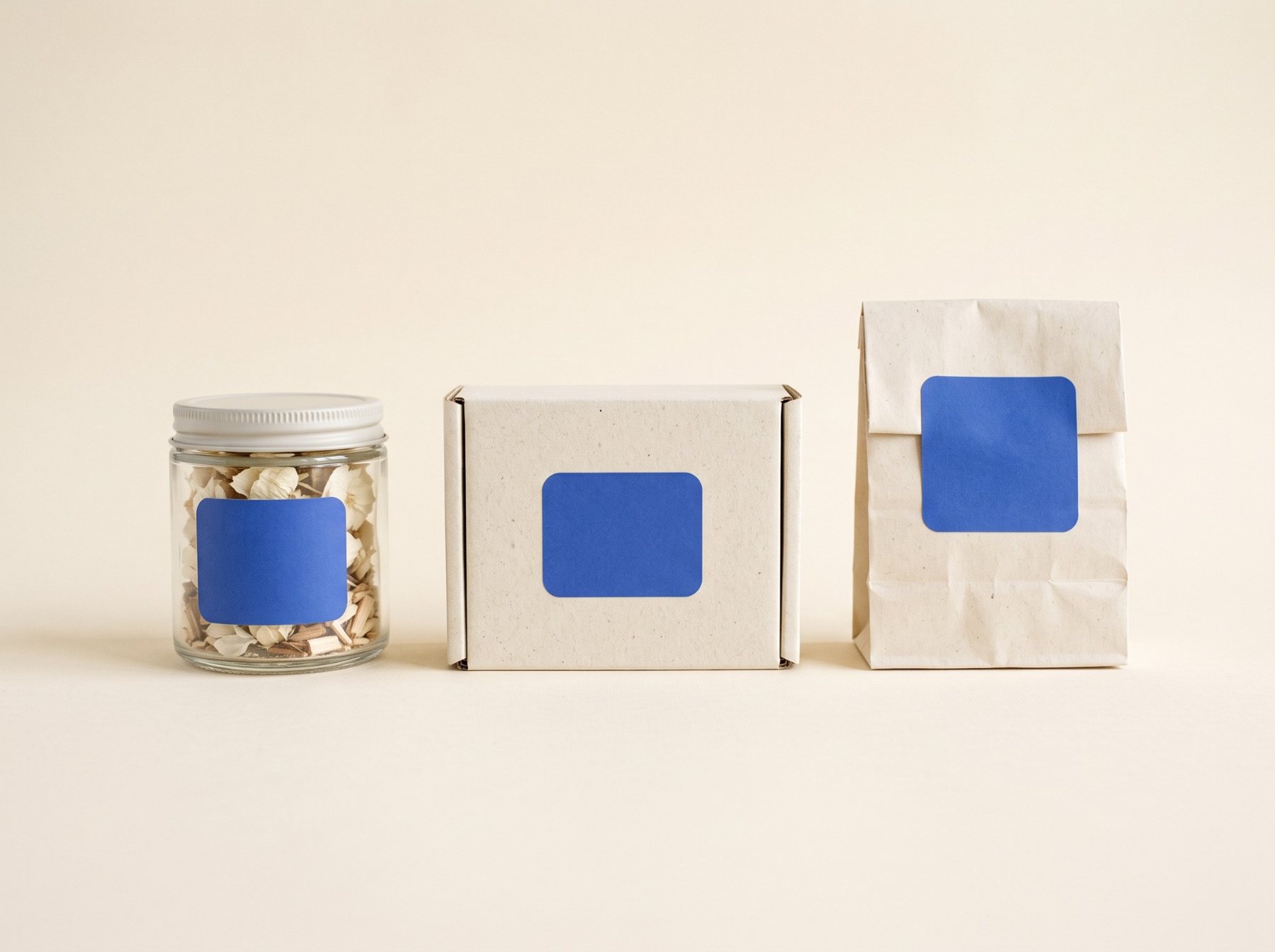 A glass jar, a box and a paper bag, each with a blank blue label